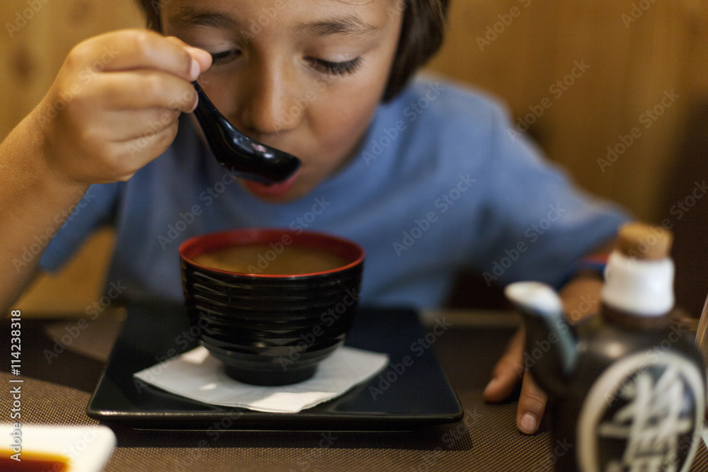 Little boy sitting in an Asian restaurant eating hot miso soup Little boy sitting in an Asian restaurant eating hot miso soup
