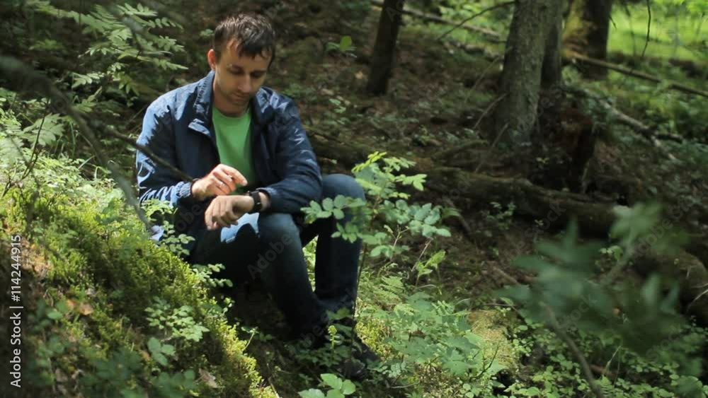 The man in the forest touc smartwatch. It sits on a small cliff green