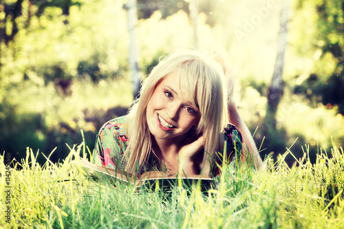 Blonde young woman girl relaxing in a park reading book, sitting alone on grass photo