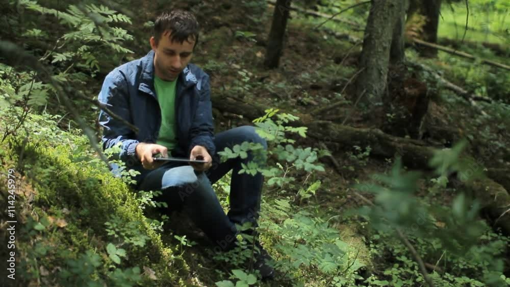 The man in the forest play on tablet in game. It sits on a small cliff green The man in the forest play on tablet in game. It sits on a small cliff green