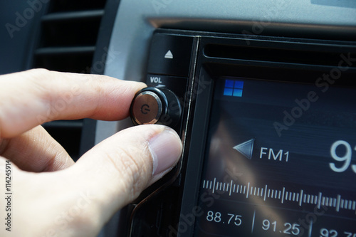 Left hand adjusting a volume control knob of the car's audio system.