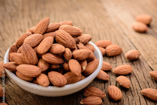 almonds in a white ceramic bowl on grained wood background