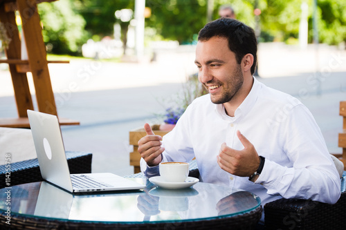 Work and relax. Online conference. Businessman dressed in shirt working with laptop, talking by skype at the park cafe outdoors photo