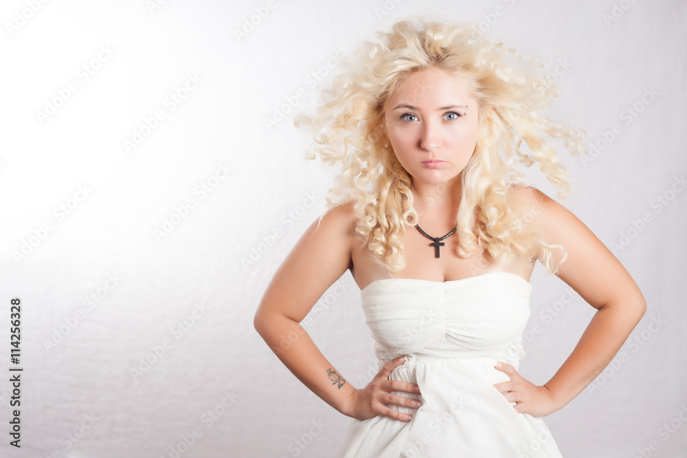 Handsome young woman in white dress with curly hair looking seriosly with cross on her neck. Blonde girl with sensual lips and beautiful blue eyes. Handsome young woman in white dress with curly hair looking seriosly with cross on her neck. Blonde girl with sensual lips and beautiful blue eyes.