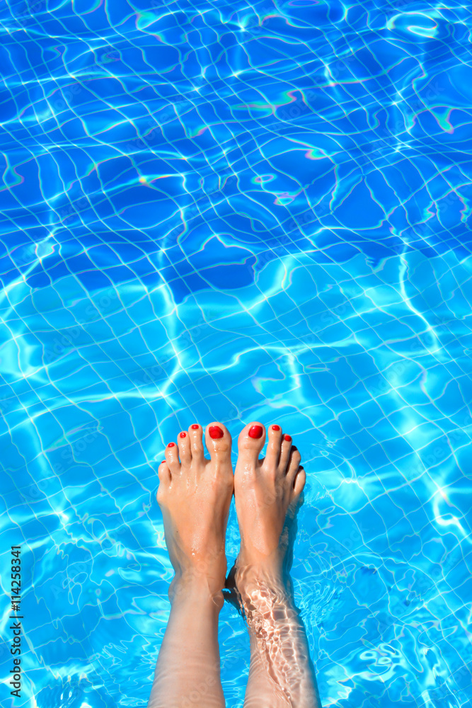 Woman feet in swimming pool on a hot summer day