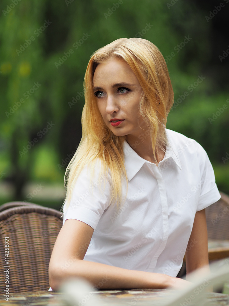 Beautiful young woman in white dress sitting at the cafe table a Beautiful young woman in white dress sitting at the cafe table a