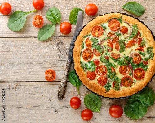Summer outdoor tart, pie of fresh vegetables - tomatoes, spinach and red onion with cream and cheese. Selective focus.  Top view. Copy space
