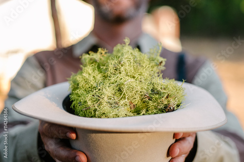 Man holding hat filled with leafy green vegetable