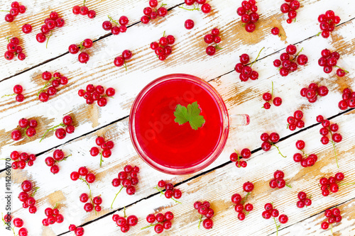 freshly squeezed red juice with green leaf currant and bunches of redcurrants on a white wooden table with old paintt. closeup flat lay photo