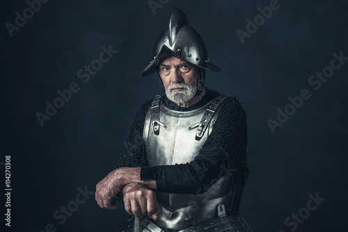 Senior knight in armor holding sword.