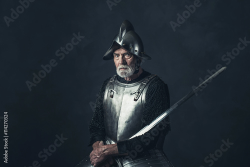 Senior knight in armor holding sword.