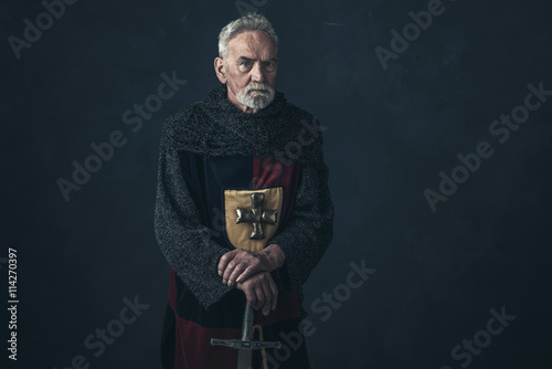 Senior knight in hauberk standing with sword.
