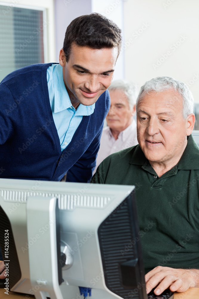 Teacher Assisting Senior Man In Computer Class Teacher Assisting Senior Man In Computer Class