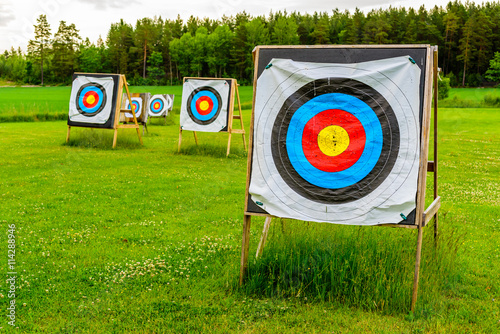 Outdoor archery targets on grass field surrounded by forest in the summer evening.