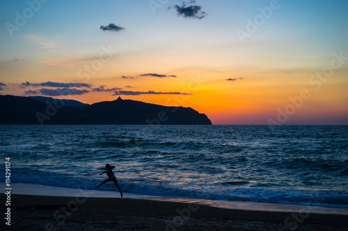 Fototapeta Naklejka Na Ścianę i Meble -  Sunrise at Tinderi beach with a girl jumping in the foreground