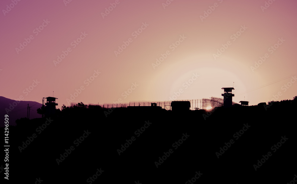 Silhouette of barbed wires and watchtower of prison in Neapolis, Crete, at sunset 