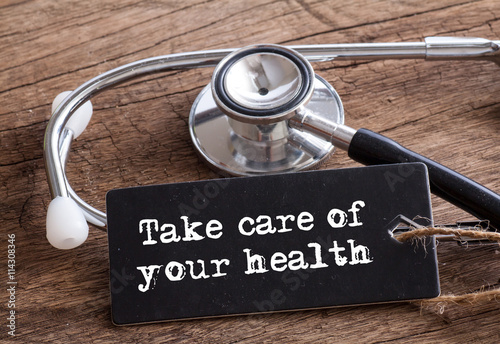 Take care of your health words written on label tag with Stethoscope on wood as medical concept