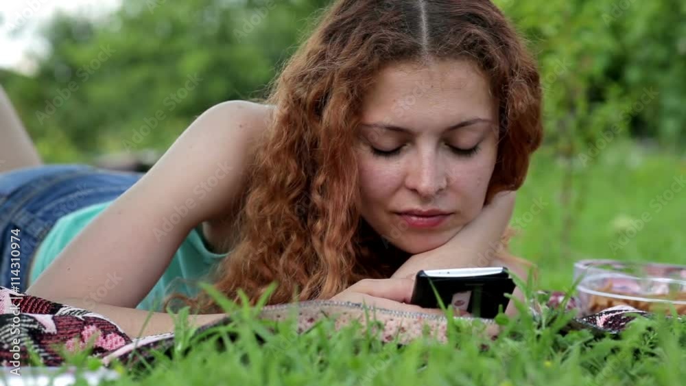 Young woman using mobile phone and lying on the green grass
