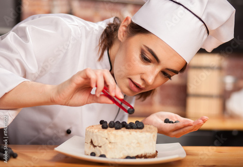 Canvas Print young woman chef cook preparing a sweet cake in the kitchen, putting blueberries