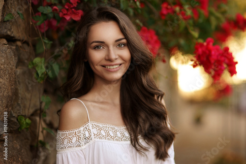 Closeup beauty portrait of young pretty happy smiling girl with dark curly hair looking at you. Soft sunset backligth photo