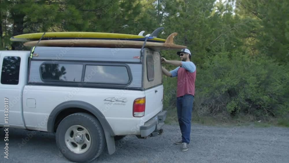 Handsome Bearded Man in sunglasses prepares to get surfboards off his white truck Handsome Bearded Man in sunglasses prepares to get surfboards off his white truck