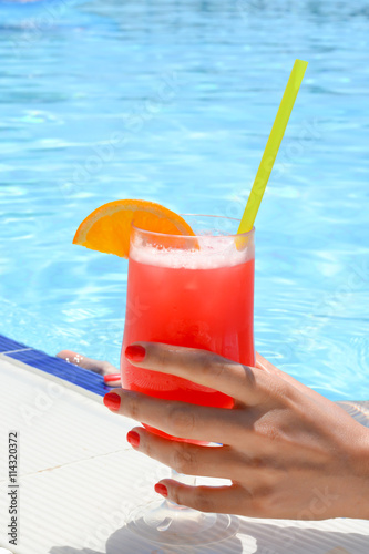 Hand holding a cocktail near a swimming pool