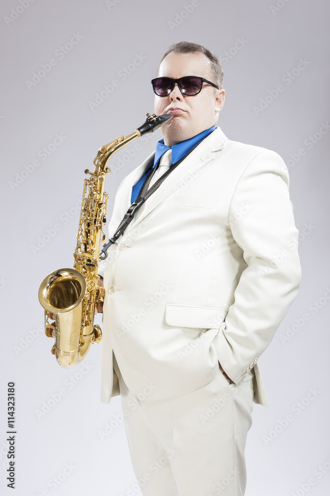Fototapeta premium Handsome Male Saxo Player in Stylish White Suit and Sunglasses Posing Against White