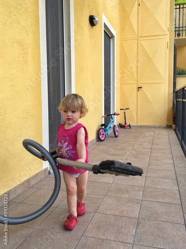 bambina con aspirapolvere sul balcone di casa photo