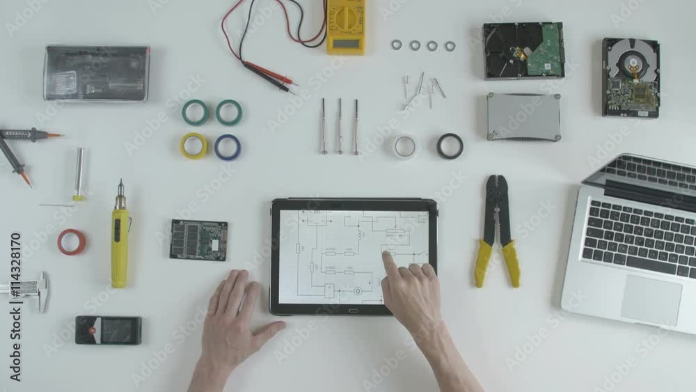 Top view software developer engineer looking at the circuit board drawing on his tablet and is planning further development of its software. Top view software developer engineer looking at the circuit board drawing on his tablet and is planning further development of its software.