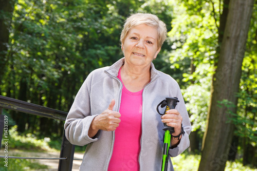 Elderly senior woman holding nordic walking sticks and showing thumbs up © ratmaner