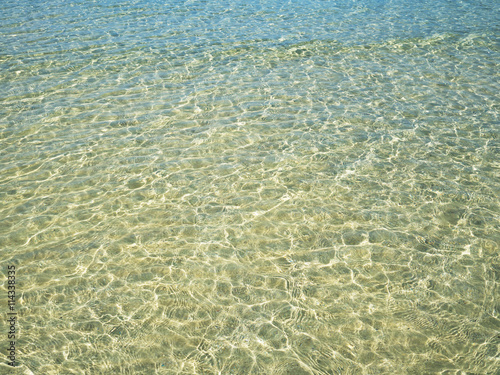 Background of transparent crystal green blue sea water surface ripple with sun reflection in summer. Water background. Ocean water texture.