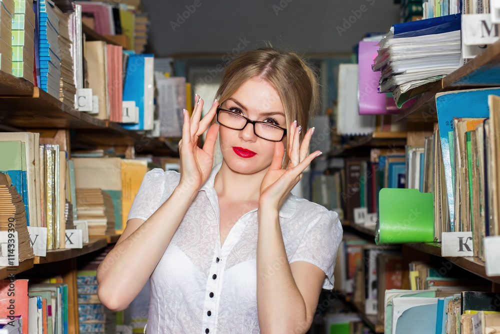 GIRL IN THE LIBRARY BETWEEN racks with books, a beautiful blonde GIRL IN THE LIBRARY BETWEEN racks with books, a beautiful blonde
