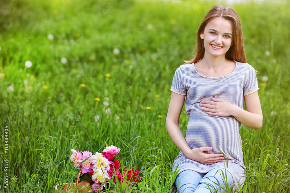 Pregnant woman with peony bouquet sitting on grass Pregnant woman with peony bouquet sitting on grass