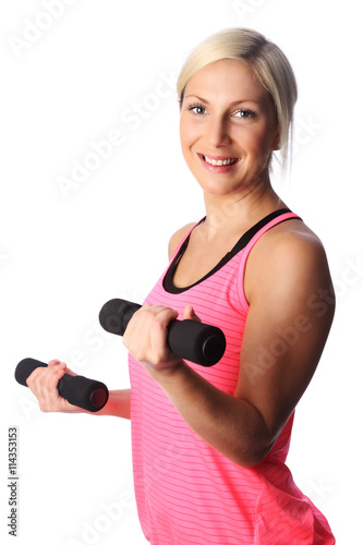 An attractive woman in a pink top standing against a white background doing barbell curls with weights. Smiling towards camera.