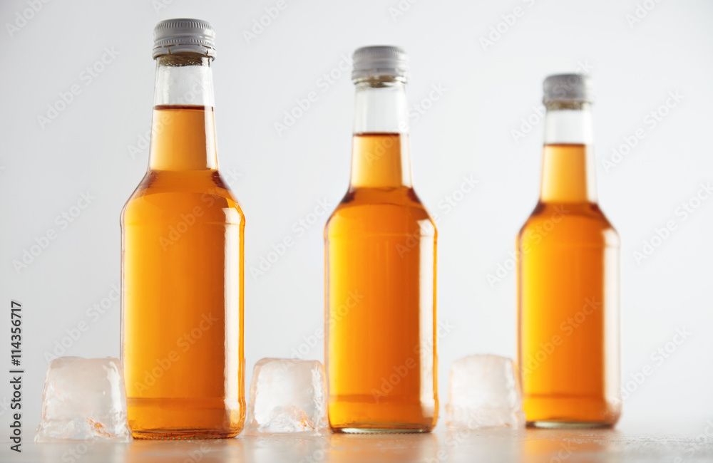 Unlabeled rustic bottles sealed with tasty cold drink inside presented next big ice cubes, isolated on white, retail mockup presentation