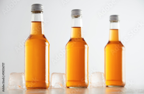 Unlabeled rustic bottles sealed with tasty cold drink inside presented next big ice cubes, isolated on white, retail mockup presentation