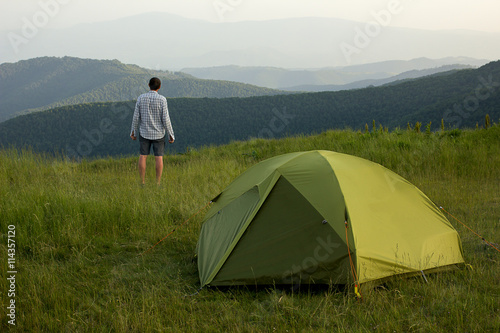 Man staying near green tent in mountains