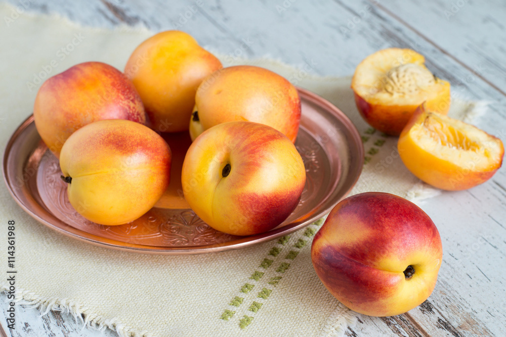  Ripe nectarines.   Ripe nectarines on a copper the tray and a napkin on a light wooden background.