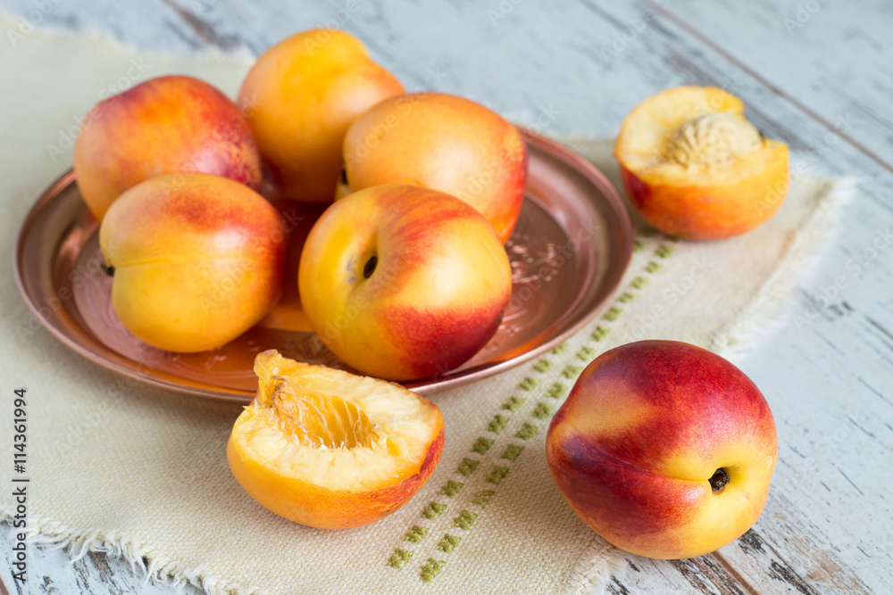 Ripe nectarines. Ripe nectarines on a copper the tray and a napkin on a light wooden background. Ripe nectarines. Ripe nectarines on a copper the tray and a napkin on a light wooden background.