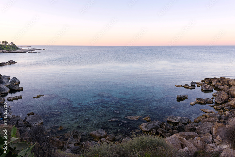 Photo of sea in protaras, cyprus island, with rocks and palm trees at sunset.