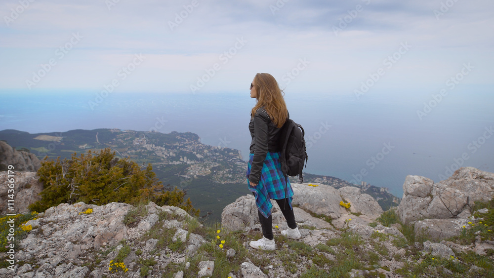 Naklejka premium Woman traveler looks at the edge of the cliff on the sea bay of mountains in the background