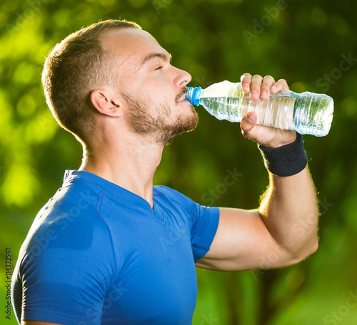 Athletic sport man drinking water from a bottle. Cold drink after outdoor fitness.