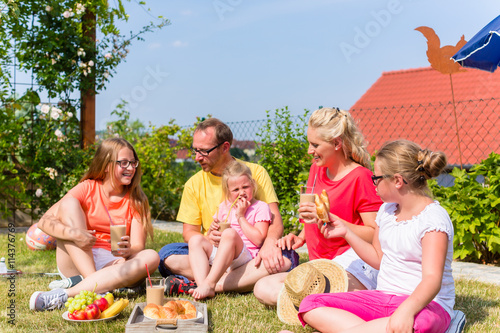 Familie isst Picknick im Garten vor ihrem Haus