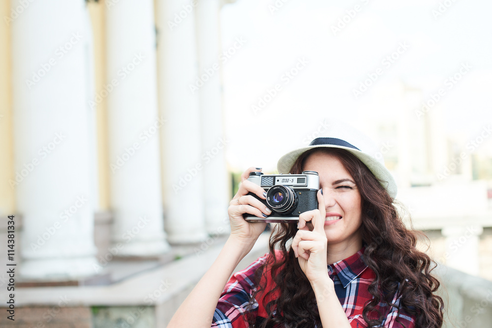 A girl tourist in a hat taking pictures of the urban landscape around the building with columns
