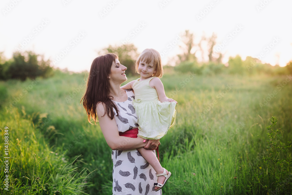 Mom kisses and hugs daughter on nature in sunset light, family, motherhood, child Mom kisses and hugs daughter on nature in sunset light, family, motherhood, child