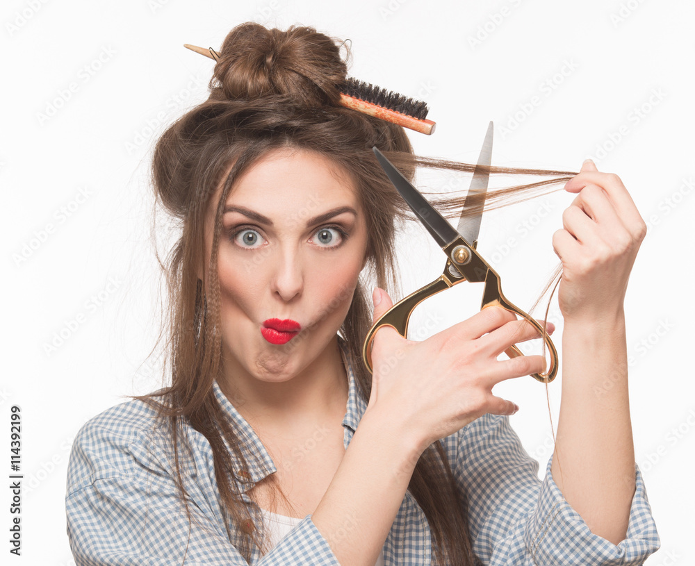 Obraz premium Portrait of beautiful woman with red lips cutting her hair over white background. Serious lady looking at camera and holding hairdressing scissors.