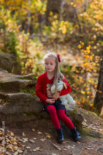 thoughtful girl sits on a rock in the autumn forest with a favorite toy in the hands of 