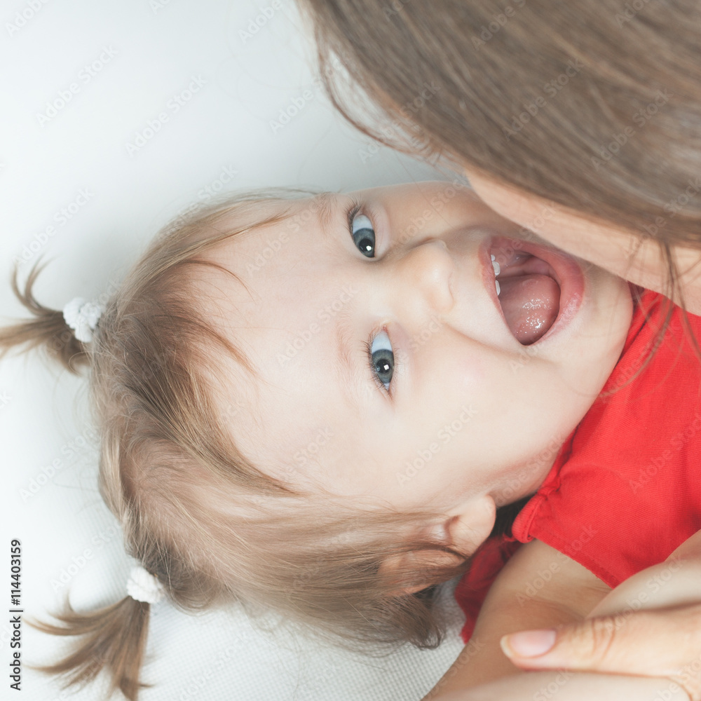 Funny baby girl lying near happy mother on white bed Funny baby girl lying near happy mother on white bed
