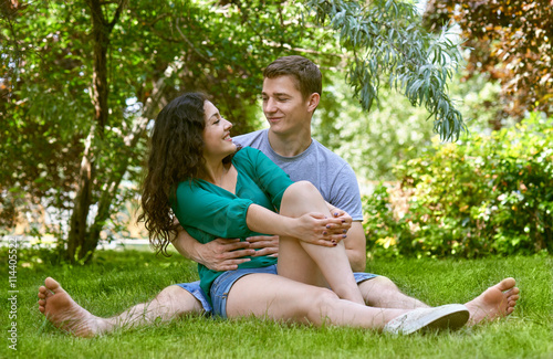 Romantic couple sit on grass in city park, summer season, lovers boy and girl