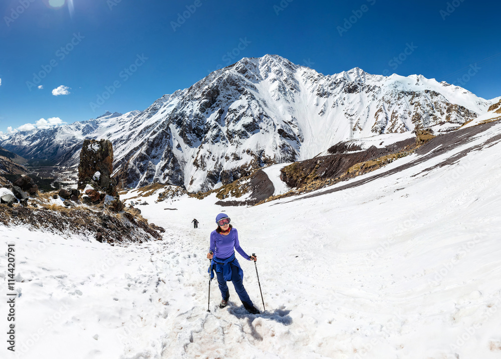 Woman hiking on sunny winter day in mountain landscape. Female hiker in warm bright outfit clothes enjoying trail walk on snow covered track.